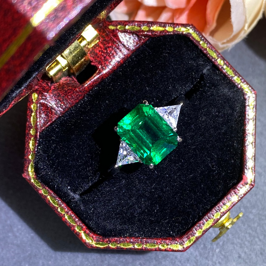 Emerald ring in a decorative box with flowers in the background