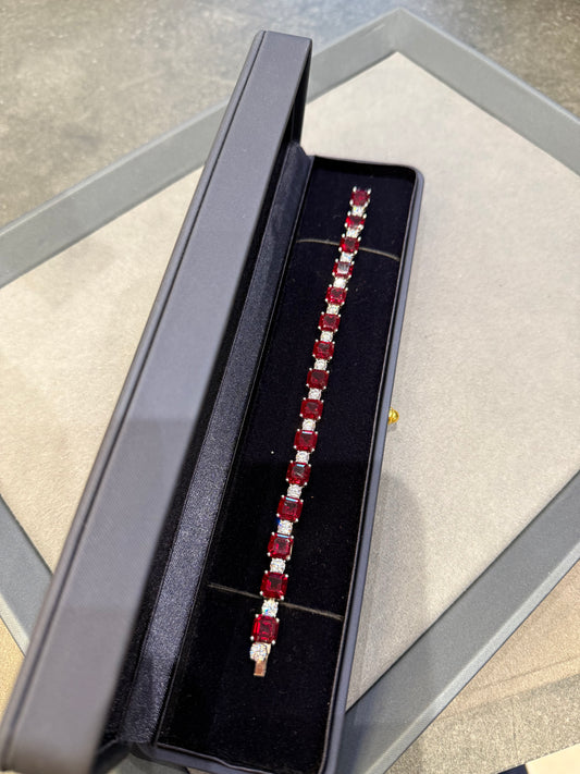 Jewelry box with a bracelet featuring red gemstones on a gray surface.