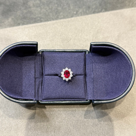 Jewelry box with a ring featuring a red gemstone and diamond on a neutral background