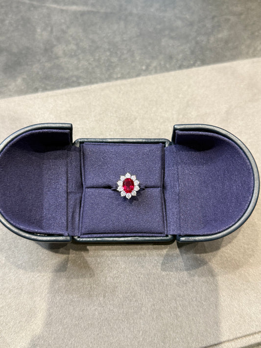 Jewelry box with a ring featuring a red gemstone and diamond on a neutral background