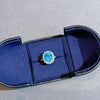 Blue gemstone ring in a blue jewelry box on a gray surface