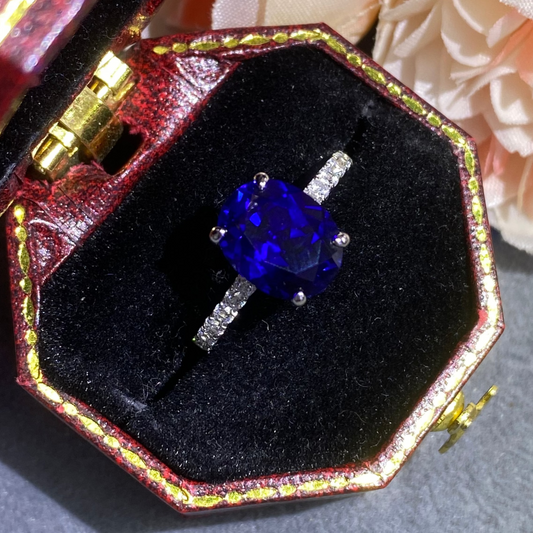 Blue gemstone ring in a decorative box with flowers in the background