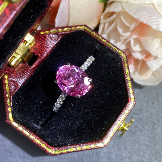 Pink gemstone ring in a decorative box with flowers in the background