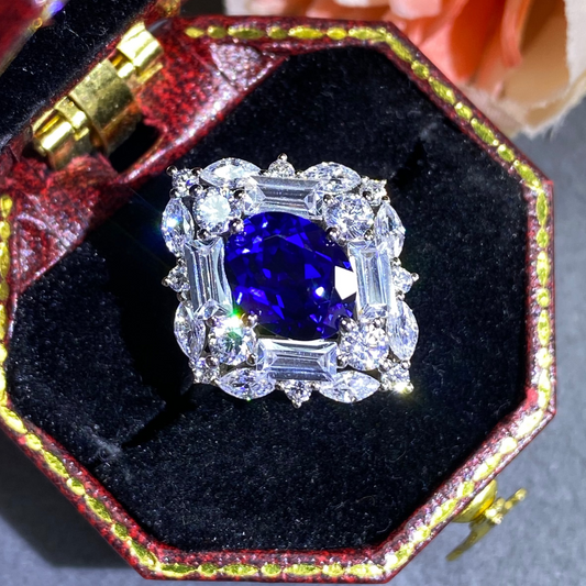 Diamond ring with a blue gemstone in a decorative box on a gray surface.