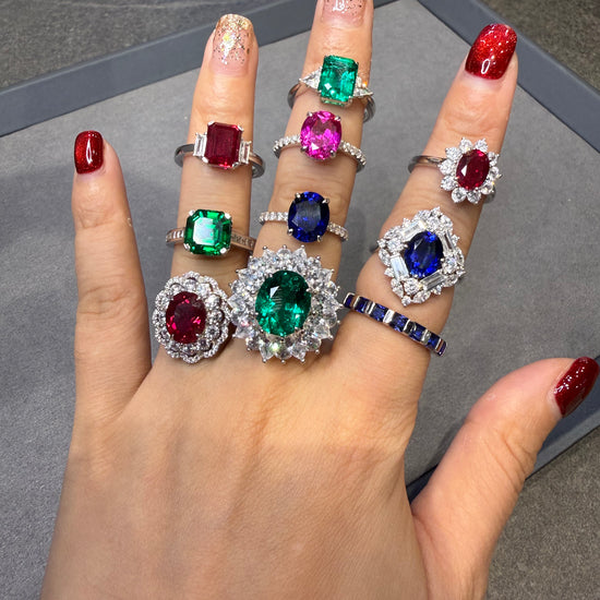 Hand wearing multiple rings with gemstones on a gray surface