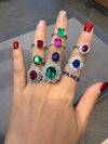 Hand wearing multiple rings with gemstones on a gray surface