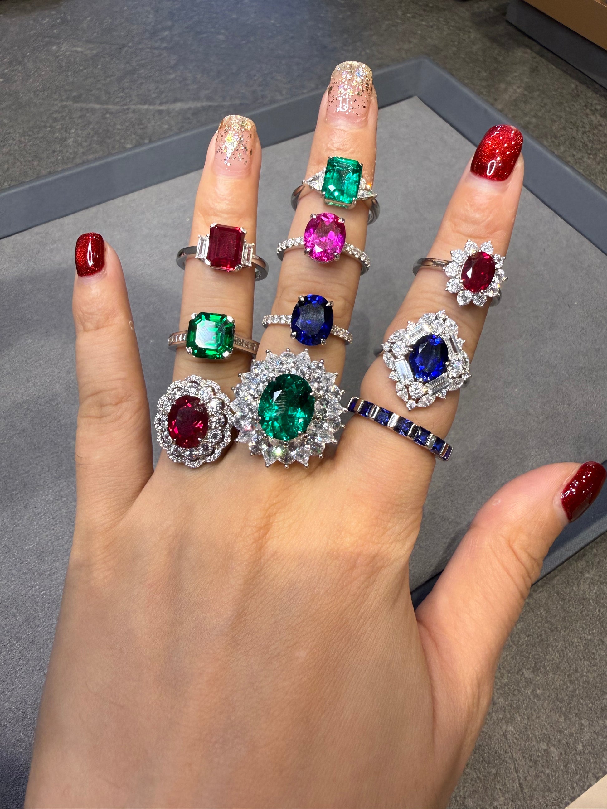 Hand wearing multiple rings with gemstones on a gray surface
