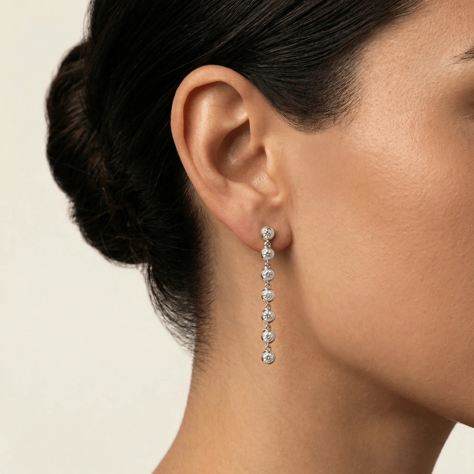 Close-up of an ear wearing a diamond earring with a neutral background