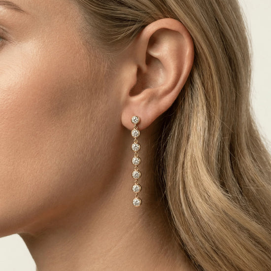 Close-up of a woman wearing gold earrings with clear stones.