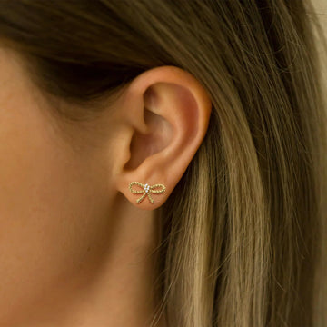 Gold bow-shaped earring worn by a person with blonde hair.