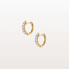 Gold hoop earrings with clear gemstones on a light beige background