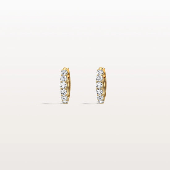 Gold hoop earrings with embedded diamonds on a light beige background