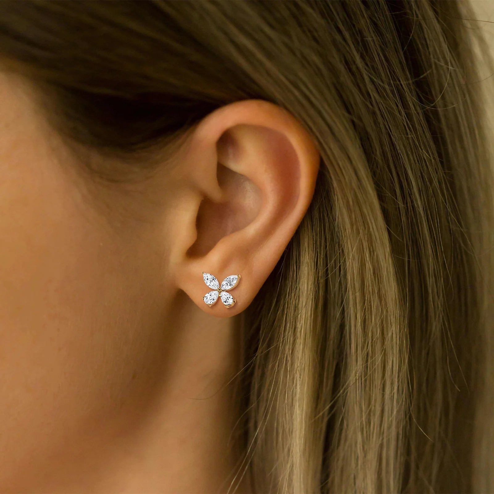 Close-up of an ear wearing a gold butterfly earring with clear stones.