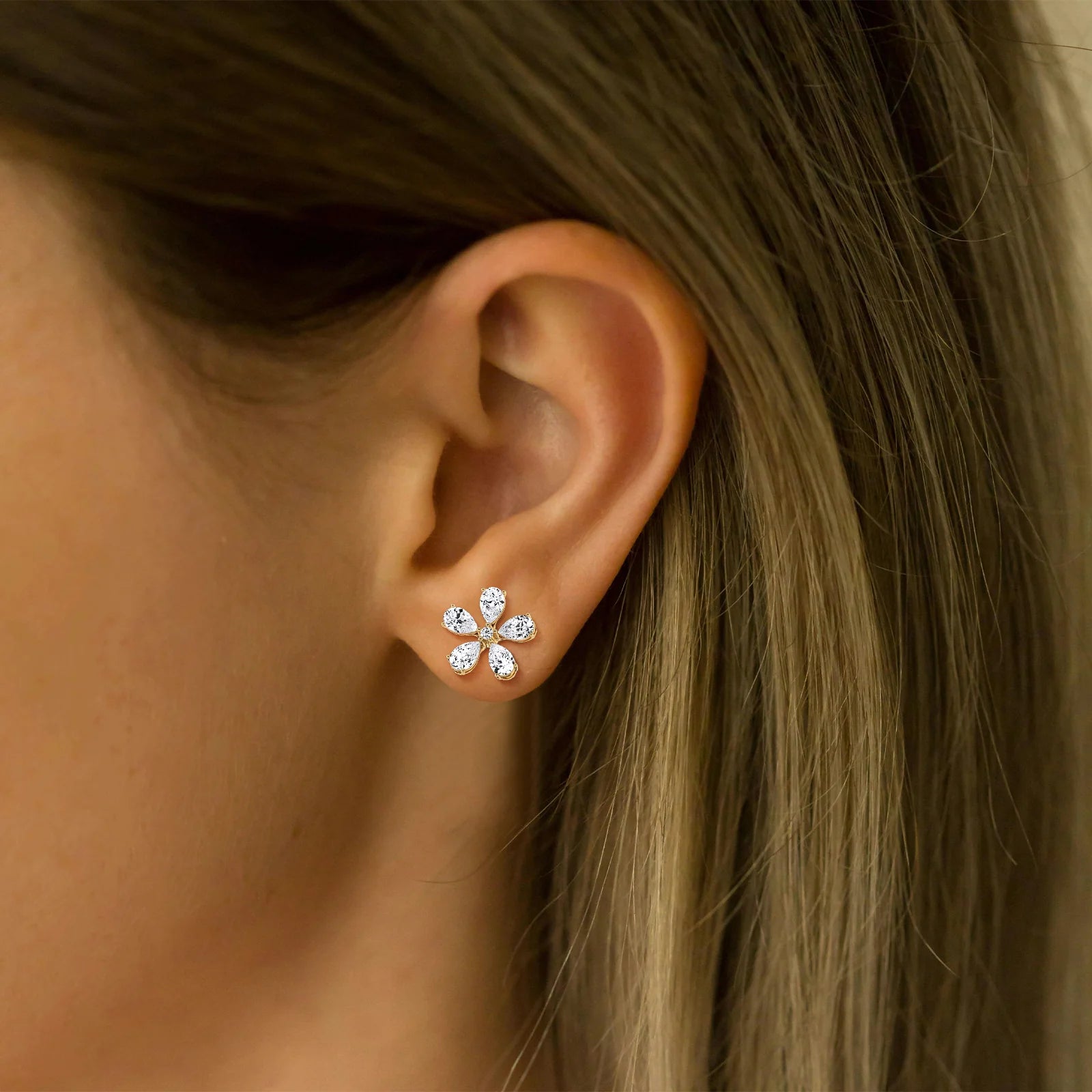 Close-up of an ear wearing a diamond stud earring with hair partially covering the frame.